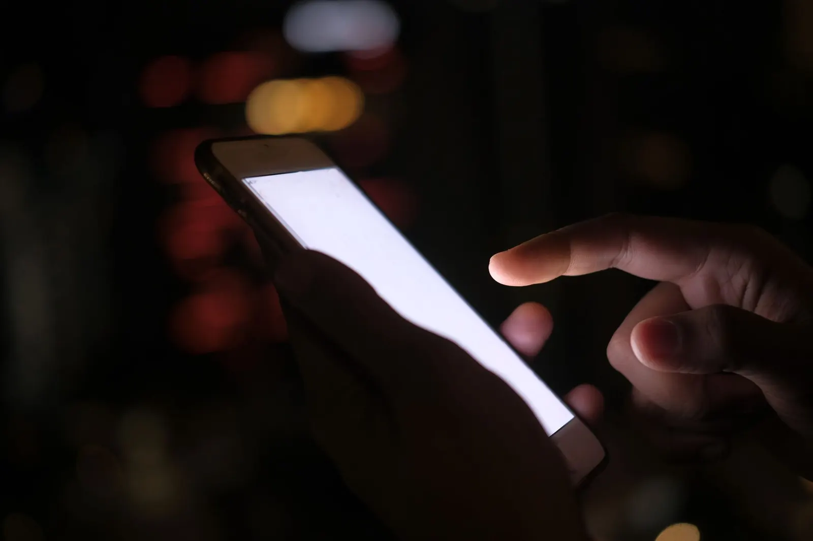 A hand tapping a glowing smartphone screen in the dark, with blurred city lights behind