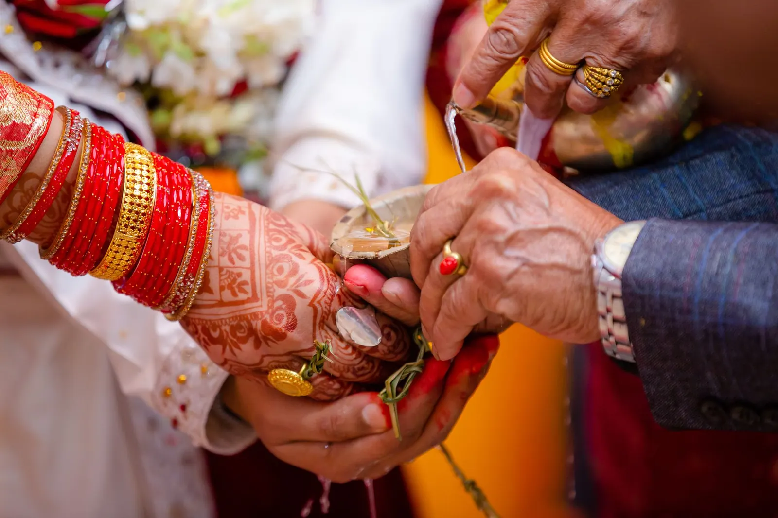 A bride's hennaed hands in red bangles held by elders' hands during a Hindu wedding ritual