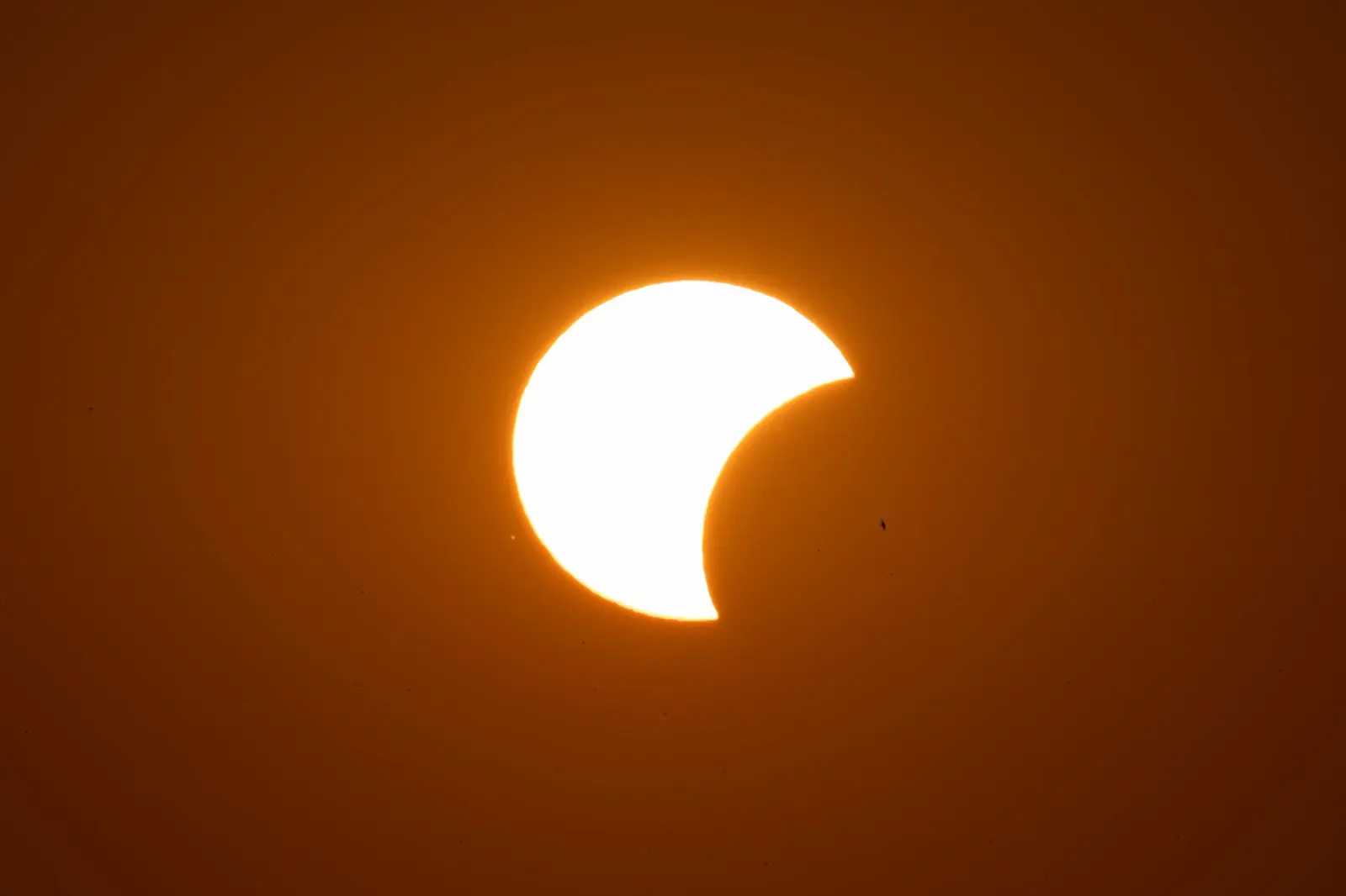 A partial solar eclipse: the Sun with a dark bite taken out of one side, glowing against an orange sky