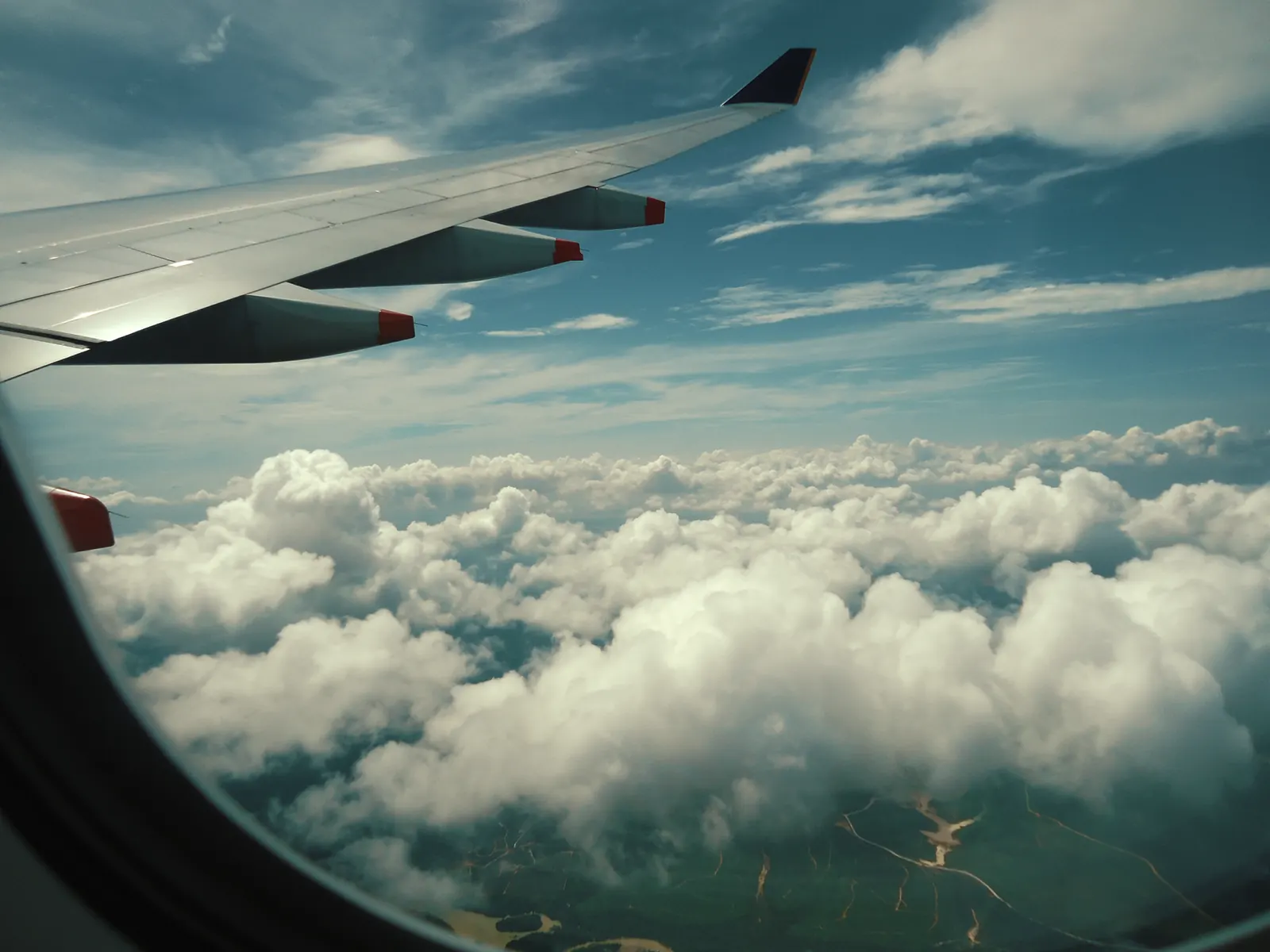 An aircraft wing above white clouds, seen through a plane window