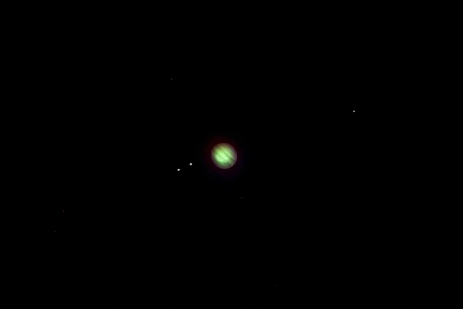 Jupiter seen through a telescope as a small banded disc, with three of its moons as dots beside it