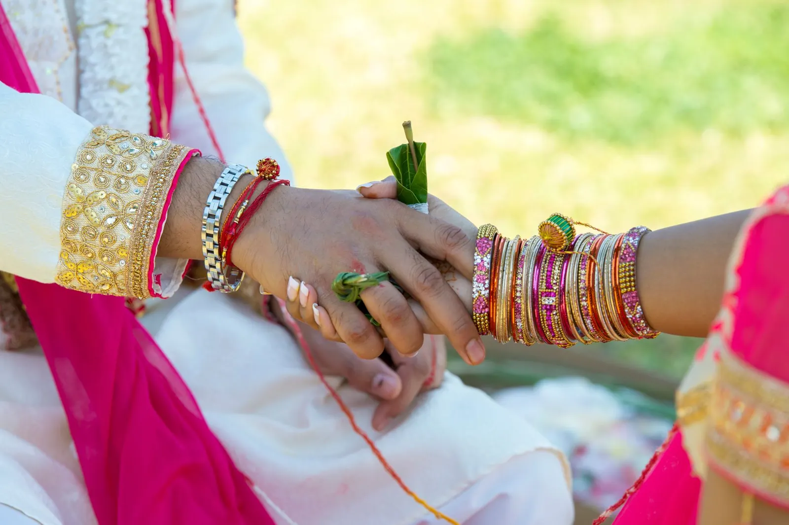 A bride's and groom's hands joined during an Indian wedding ritual, her wrist full of coloured bangles