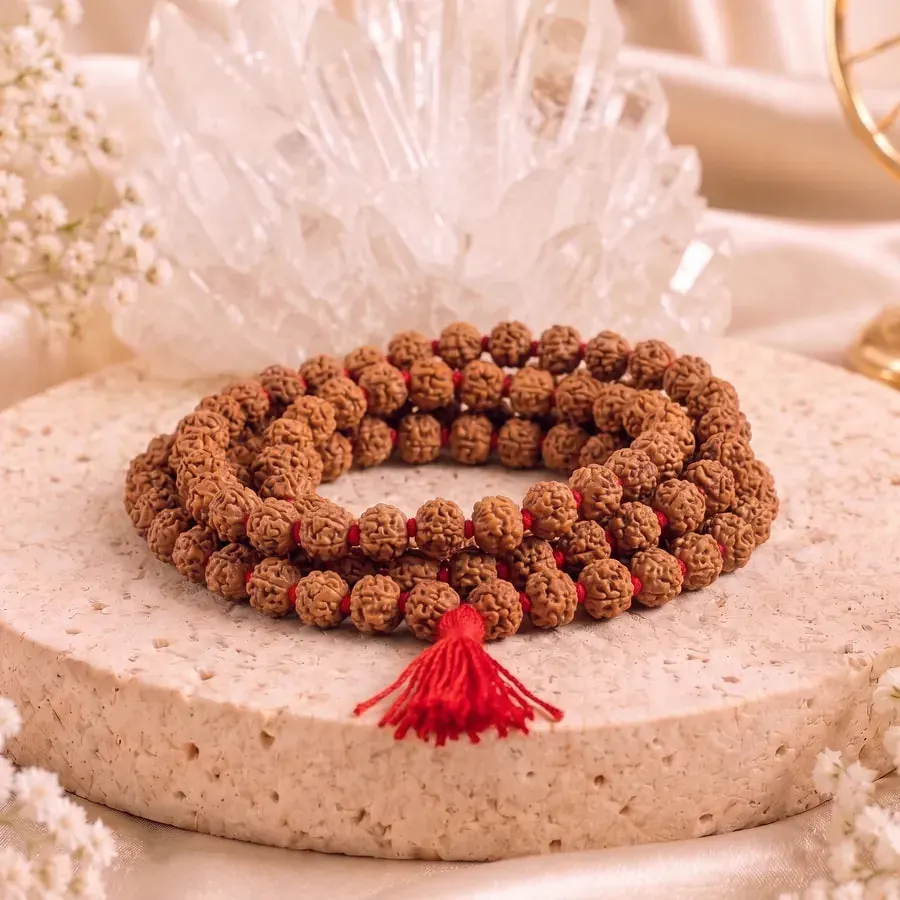 A coiled rudraksha mala knotted with red thread, with a red tassel at the guru bead, on a round stone
