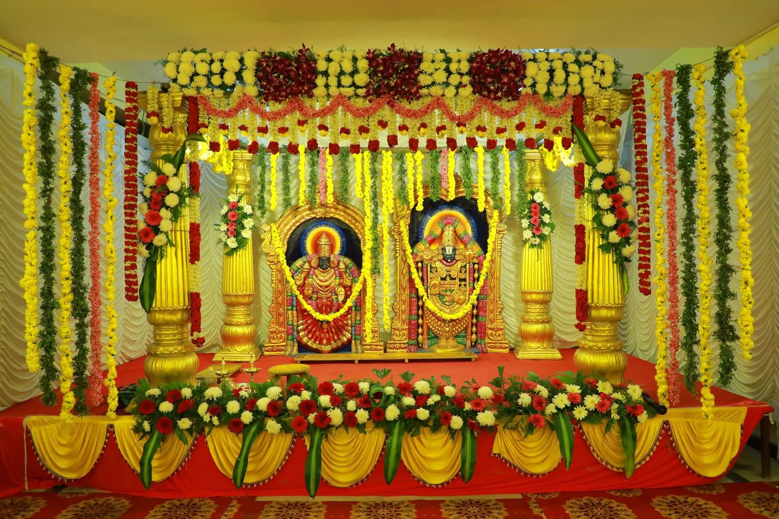 Indian wedding stage with marigold and rose garlands, gold pillars and two framed deity images
