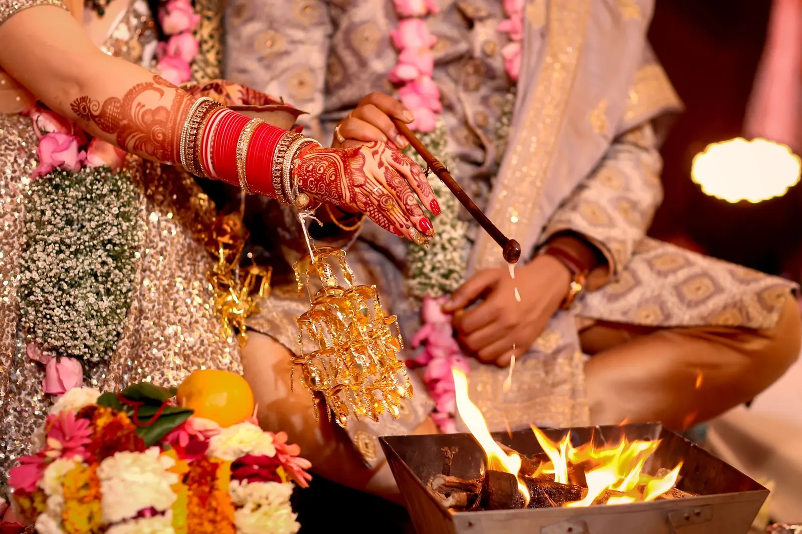 A bride's hennaed hand with red bangles pouring an offering into the sacred fire at a Hindu wedding