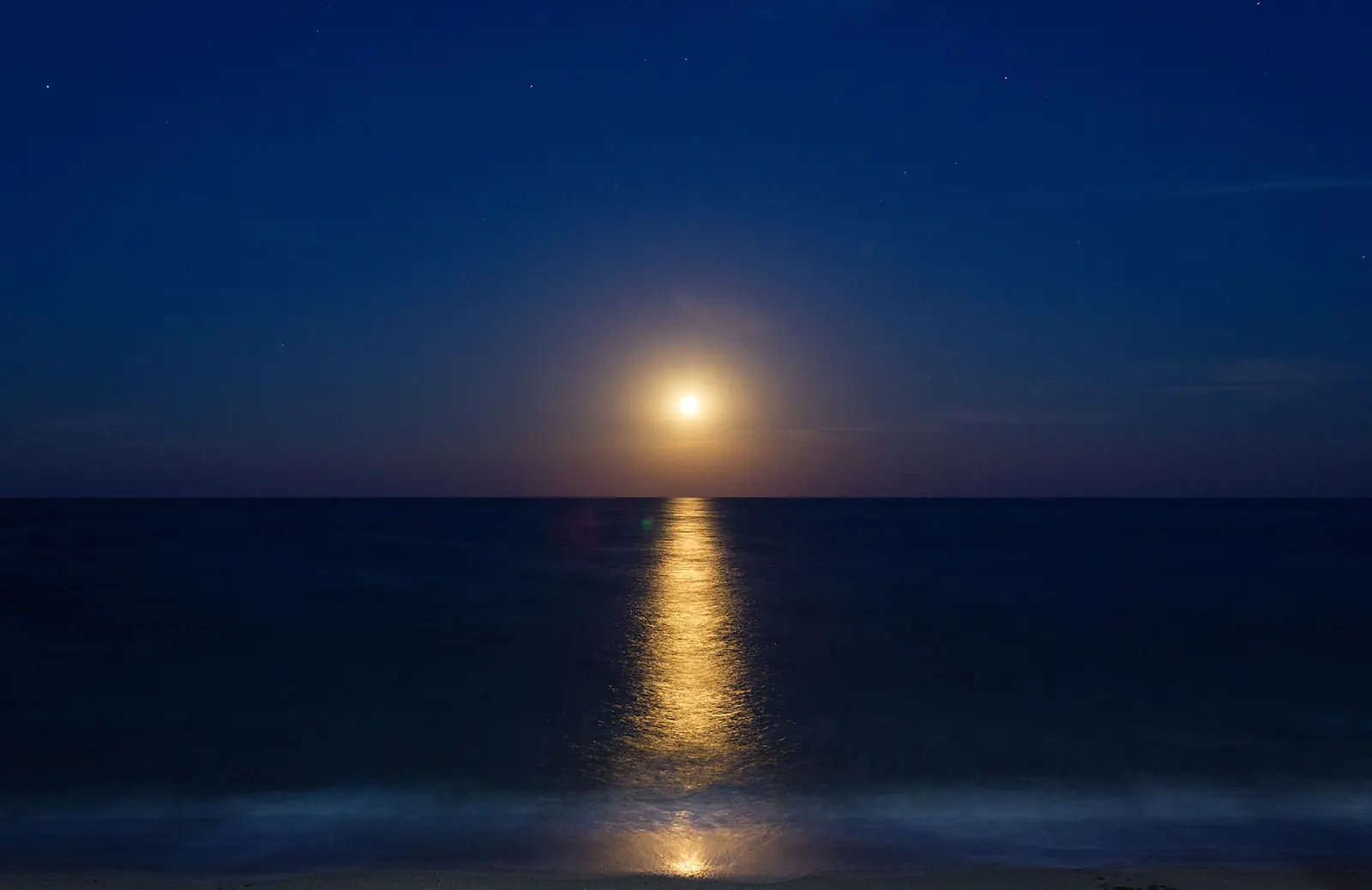 A low moon over a calm sea at night, its light making a path on the water