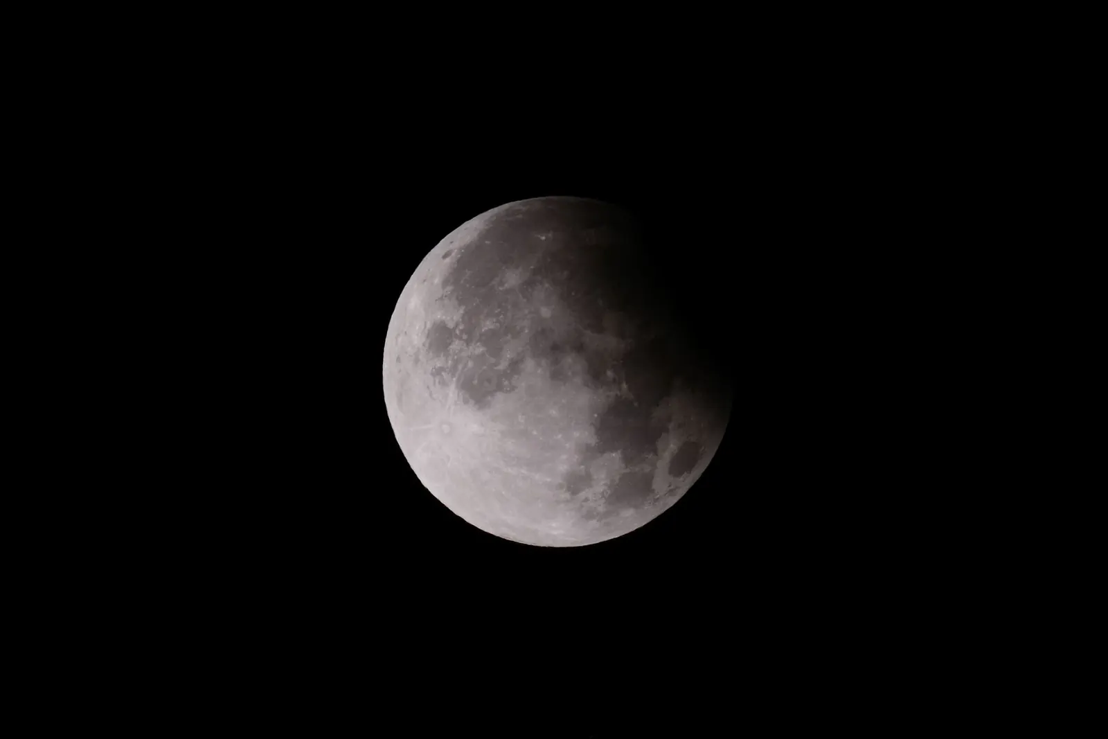 The Moon in partial eclipse against a black sky, its right side darkened by Earth's shadow