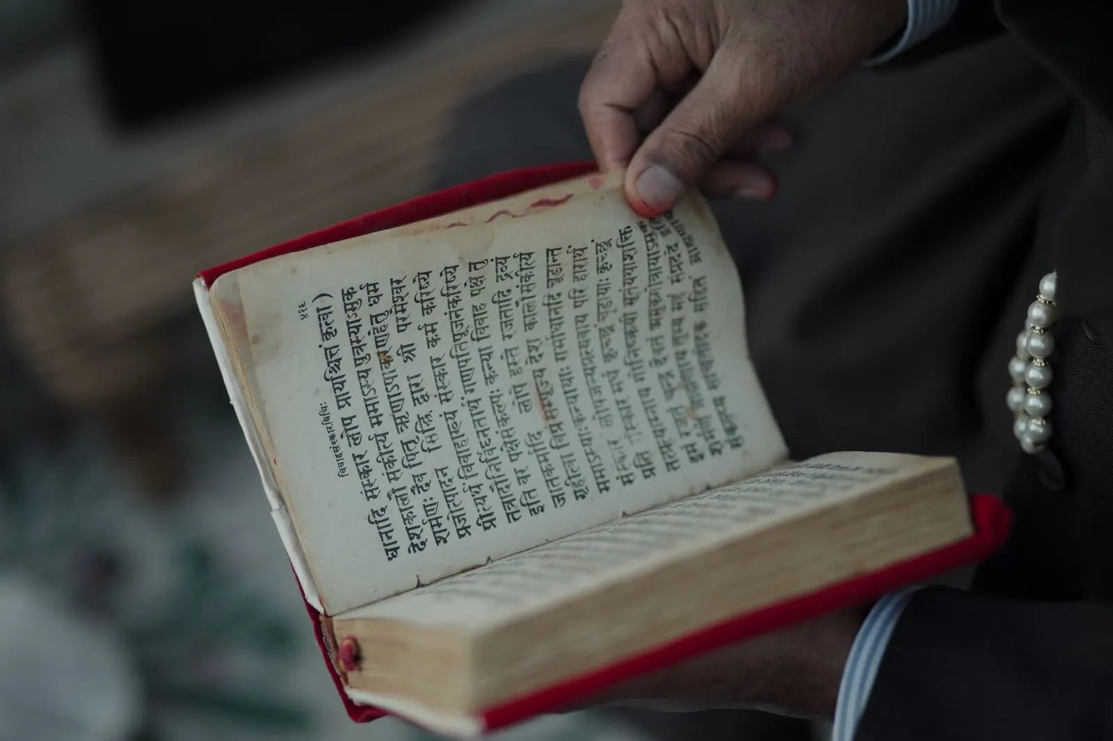 Hands holding an old open book printed in Devanagari script with red edges