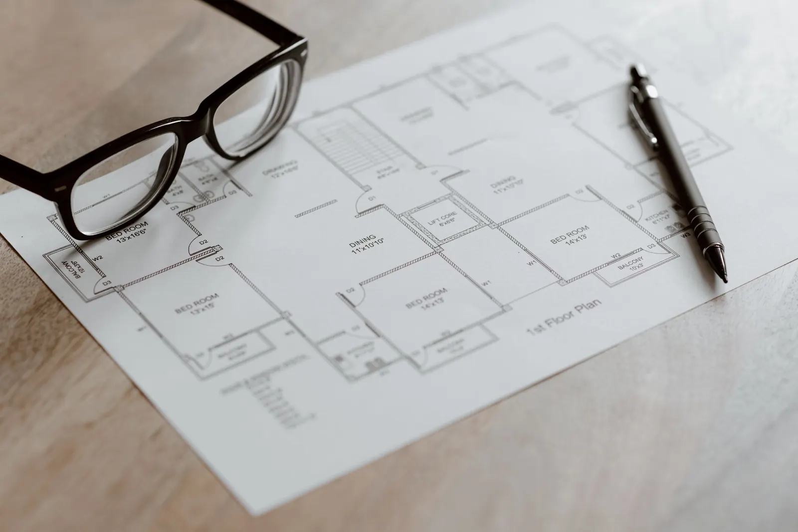 A printed floor plan of a home with bedrooms marked, glasses and a pen on a wooden table