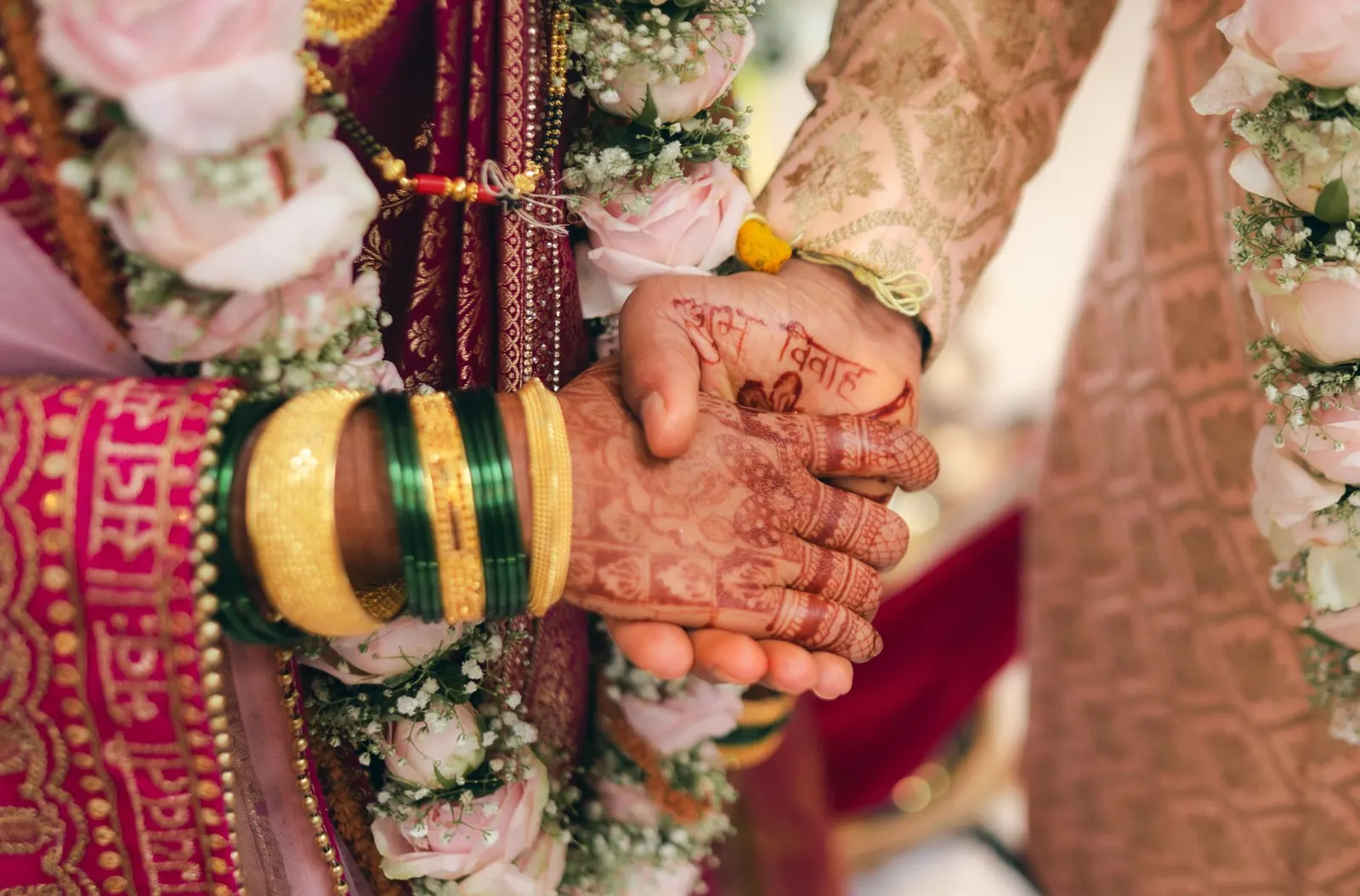 भारतीय शादी में दूल्हे के हाथ में दुल्हन का मेहंदी लगा हाथ, साथ में फूलों की मालाएँ और चूड़ियाँ