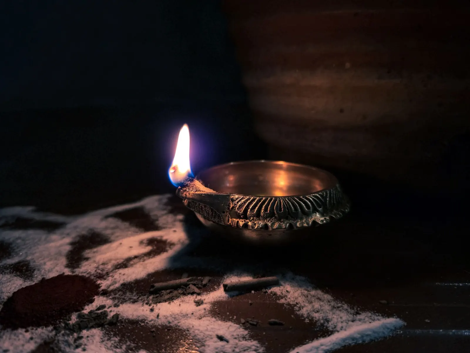 A lit brass oil lamp (diya) with a single flame in a dark room