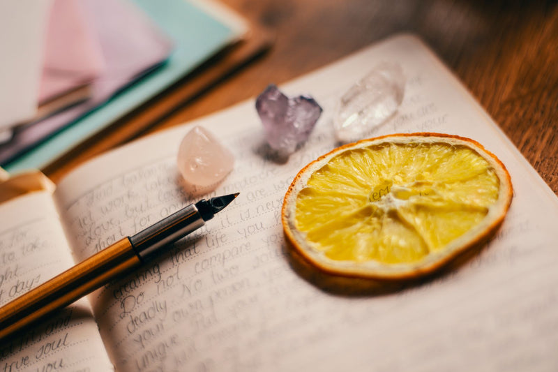 Purple amethyst and green aventurine bead bracelets lying beside an open notebook and a pen on a wooden desk