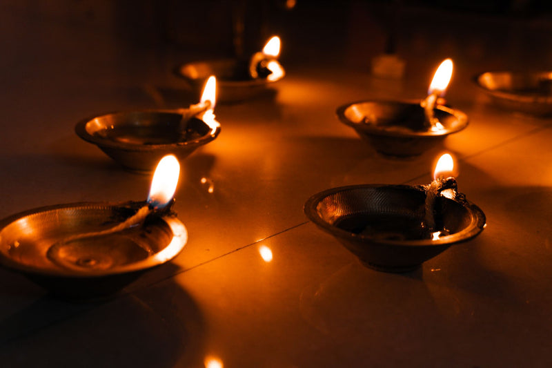 Lit brass diya lamps arranged beside an orange marigold garland on a wooden surface