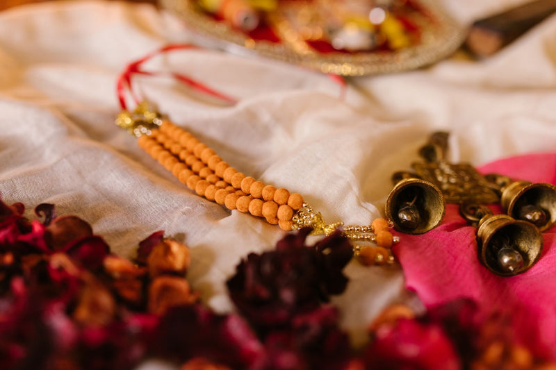 Brown rudraksha beads laid on red cloth beside a lit brass diya and scattered marigold petals