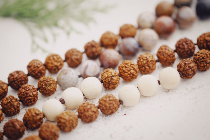 Two white howlite bead bracelets beside a rudraksha bead on a warm wooden table lit by a candle